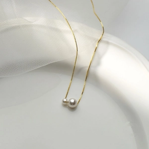 Detail view of gold dual-pearl pendant necklace on white ceramic tray with soft tulle background