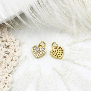 Macro view of gold heart pendants with micro-pave crystals on soft feather background