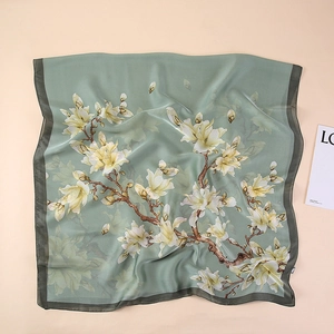 Detail of elegant bean green silk scarf featuring classic white magnolia floral prints