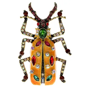 Vintage enamel beetle brooch with orange wings and green crystal stone on white background