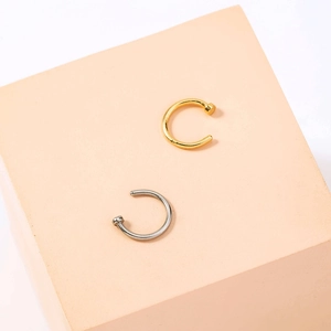 Macro shot of gold and silver U-shaped nose rings displayed on a soft peach pedestal