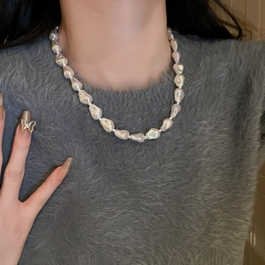 Close-up of elegant baroque white irregular pearl necklace worn over a grey sweater