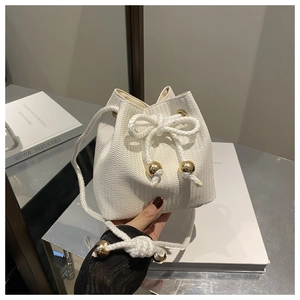 Dettaglio della borsa a secchiello intrecciata bianca con sfere dorate e coulisse in corda