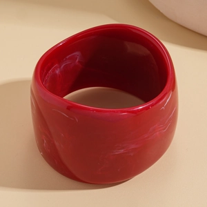 Macro detail of a wide red resin bangle with white marble texture on beige leather
