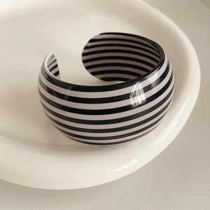 Close-up of black and white striped wide open cuff bangle on a white ceramic plate