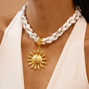 Close-up of a large gold sun pendant on a textured white woven cord necklace