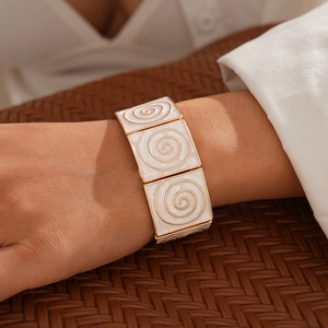 Detailed close-up of retro white enamel square tiles with golden spiral patterns on a wide bracelet