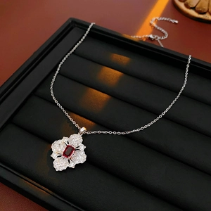 Detailed close-up of a silver flower necklace with a red gemstone and crystal inlay