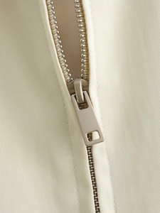 Dettaglio macro della zip in metallo e del tessuto twill su una giacca beige donna