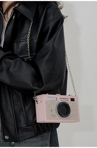 Pink leather camera-shaped crossbody bag with rhinestones and chain strap on a model