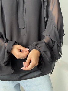 Close-up of black chiffon blouse detail showing ruffled layers and tiered bell sleeves