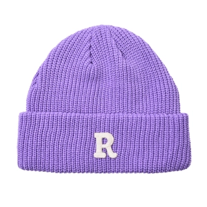 Dettaglio del berretto in maglia viola con toppa della lettera R bianca e bordo arrotolato