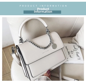 Detail of cream leather shoulder bag with silver chain and metal pendant on sofa
