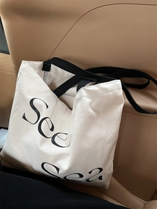 Detail view of cream canvas tote bag featuring black See Sea artistic lettering print