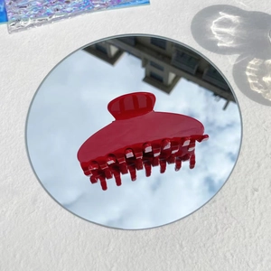 Detailed view of a glossy red hair claw clip on a mirror reflecting a clear blue sky