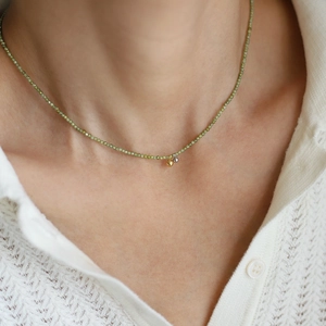Close-up of olive green beaded necklace with gold and silver zircon pendant on a model