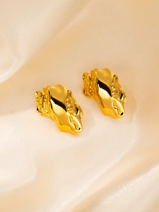 Détail de boucles d'oreilles dorées à texture de lave sur tissu satiné beige