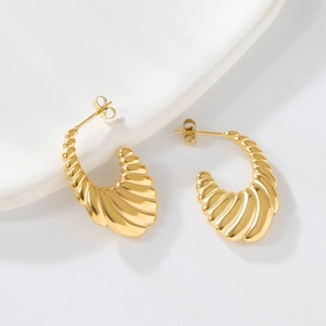 Detail of gold C-shaped croissant earrings with textured ribbed design on ceramic plate