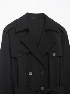 Detail shot of the lapels, shoulder straps, and buttons on a black midi trench dress