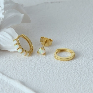 Detailed set of gold earrings with opal stones and smooth hoops on white floral background