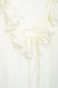 Close-up of white chiffon blouse featuring delicate ruffle V-neck and tie string detail