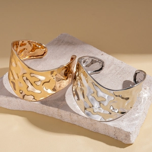 Irregular wavy textured open bangles in gold and silver finish on stone display