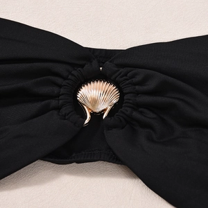 Detail of black crop top with a gold shell-shaped metal buckle and textured elastic fabric