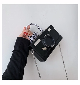 Close-up of camera-shaped crossbody bag featuring patent leather and polka dot ribbon handle