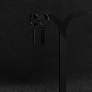 Close-up of black matte stainless steel huggie earrings with cylindrical bar pendants
