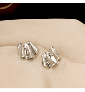 Detailed macro view of irregular silver geometric earrings on champagne silk background
