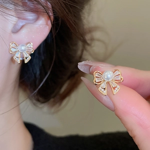 Detail of bow-shaped stud earrings with zircons and pearls on a model ear