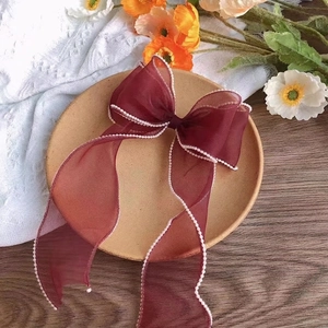 Elegant burgundy oversized gauze bow hair accessory with pearl edges on wooden tray
