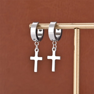 Macro detail of silver cross pendant earrings on minimalist golden display stand