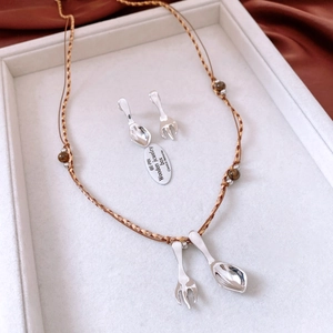 Detailed view of silver cutlery spoon and fork pendants with brown woven cord necklace
