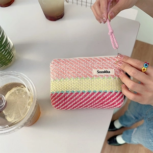 Macro detail of striped woven cosmetic pouch with pink rope zipper on a summer desk