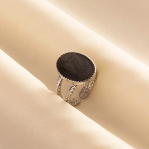 Macro shot of silver-tone twisted open ring with oval black enamel on silk background