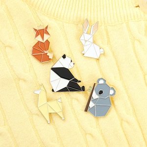 Detail of origami animal enamel pins featuring fox and panda on yellow knitted fabric