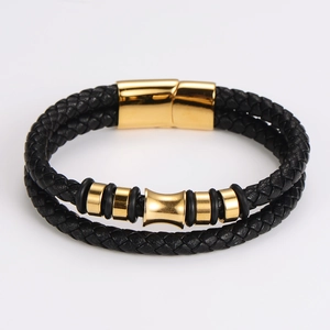 Detalle de pulsera de cuero trenzado negro con cierre magnético dorado y adornos de cilindro