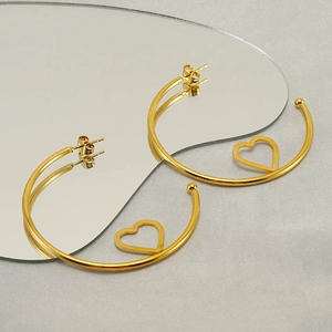 Detail view of gold-tone C-shape hoop earrings with hollow heart charms on grey fabric