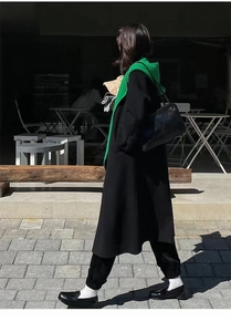 Detail view of a stylish green hooded scarf and shawl paired with a long black winter coat