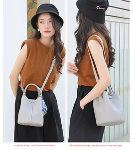 Light grey bucket bag detail with interchangeable dual straps and silk scarf accent