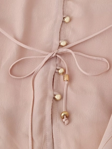 Dettaglio di camicetta in raso rosa con bottoni dorati ed elegante fiocco frontale