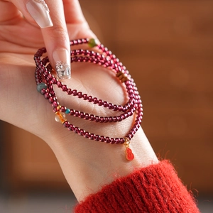 Close-up of garnet multi-wrap bracelet with red enamel gourd charm on a female wrist