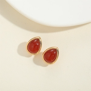 Minimalist red teardrop stone earrings with gold metal frame on a soft textured base