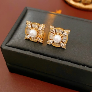 Close-up of golden square stud earrings with central pearl and zircon accents