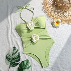 Flat lay of light green cutout swimsuit with white rose flower detail and summer props