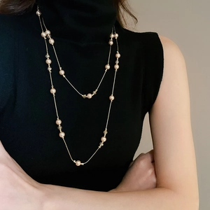Collier double rangée dorée avec perles et cristaux sur un pull noir à col roulé