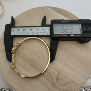 Detailed measurement of golden clover bracelet inner diameter showing 52.3mm on digital caliper