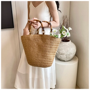 Detailed close-up of a large straw tote bag featuring authentic polished bamboo handles