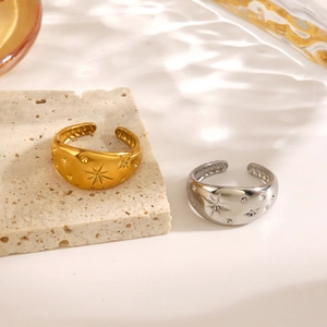 Adjustable gold and silver starburst rings with zircon accents on stone surface